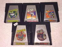 Five Atari game cartridges shown on carpeted surface, each with distinct label art for Frogger, Star Wars The Empire Strikes Back, Super Cobra, Popeye, and Star Wars Jedi Arena.
