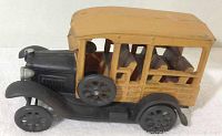 Side view of a cast metal toy car with wood-colored passenger compartment and black metal frame and wheels, showing detailed seats and spare wheel.