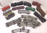 Full overhead view of the lot showing multiple O scale vintage train cars and metal tracks spread out on a white surface.