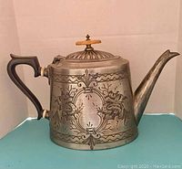 Full side view of the Victorian engraved pewter teapot with wooden handle and lid knob, showing the overall form and engraving details.
