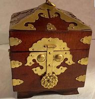 Exterior front and top view of a square wooden box with brass hardware and lock.