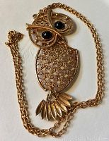 Full view of gold-tone owl necklace showing front filigree design, black cabochon eyes, and chain.