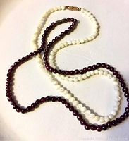 Overview photo showing two beaded necklaces, white mother of pearl beads and dark red garnet beads, arranged on a flat surface.
