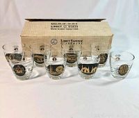Lot of eight vintage 1964 New York World's Fair highball glasses in front of original Libbey Safedge Glassware box. Glasses are clear with black and gold designs.