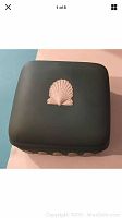 Top view of square dark teal box with a single raised white seashell decoration on the center of the lid.