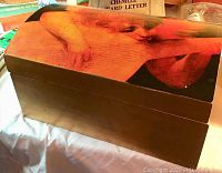 Large wooden box with dome lid featuring cherub artwork in warm tones, closed state
