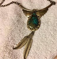 Close view of the turquoise stone set in hammered sterling silver with fan detail and two hanging silver feathers on chain.