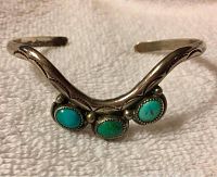 Front view of sterling silver cuff bracelet showing three bezel-set turquoise stones and engraved decorative details on the arms.