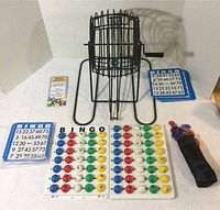Complete bingo game components with wire cage, balls on trays, bingo cards, and chips displayed