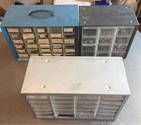 Three multi-drawer storage bins including a blue metal framed bin, a black plastic bin, and a white plastic bin shown from the outside.