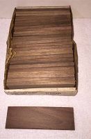 Box containing 27 rectangular walnut hobby blank planks stacked neatly, showing smooth faces and end grain.