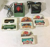 Photo showing two transformers and five N scale train cars in packaging. The Fleischmann transformer is green with a red dial. The Trainmaster transformer is black with an attached switch. Train cars include three Bachmann boxed cars labeled 'Freight Cars' and 'Old Timers' and two white plastic cars in foam packaging.
