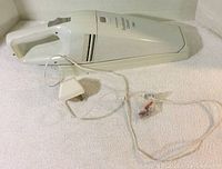 White Black and Decker Dustbuster Classic Plus handheld vacuum cleaner with attached power cord laid on white surface.