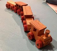Front perspective view of the wooden train set showing the locomotive and cars linked in a row on a flat surface.