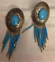 Pair of sterling silver earrings with turquoise-colored oval stones and hanging bead fringe on white background.
