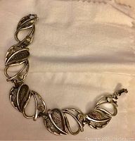 Full view of the linked leaf-shaped silver-tone bracelet laid on a light fabric background.