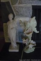 Photo showing the two angelic figurines placed together in front of a stone fireplace.