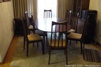 Oval walnut dining table with six chairs arranged around on carpeted floor.