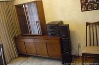 Full view of sideboard base topped by glass hutch alongside stereo speakers