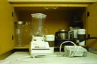 Photo showing Osterizer blender, mugs, glass jars inside a wooden cabinet