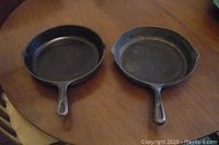 Two cast iron fry pans side by side on wooden table, showing overall size and shape.