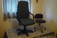 Tall gray high-back office chair with armrests and small brown armless office chair on a floral mattress.