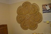 Full view of the woven mat wall hanging on a wall, showing the overall floral shape and size context.