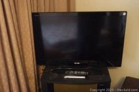 Small Sony Bravia flat screen television on black stand with remote control in front.