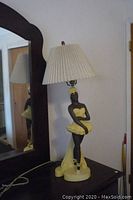 Full view of lamp showing dancer figure in yellow dress on dark base with pleated lamp shade.
