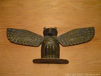 Front view of cast metal owl totem with detailed wing designs and fixed base.