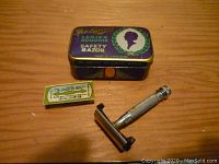 Overview of the razor, blade box, and decorative tin on wooden surface