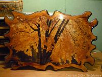 Wooden plaque with irregular natural edge featuring a decoupage fall scene with orange leaves and tree trunks.