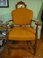 Full front view of vintage wooden chair with upholstered seat and backrest, showing carved wooden details and mustard fabric upholstery.