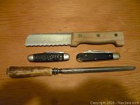 Set of three knives and one sharpening steel laid out on wood surface, showing full length and handles.