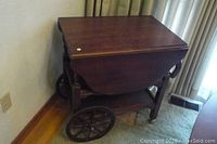 Front view of vintage walnut tea/bar cart with drop leaves closed, showing large metal wheels and turned legs.
