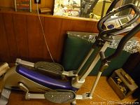 Side view showing metallic frame, foot pedals with grip, and black handlebars with a blue horizontal arm cover.