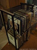 Full view of the black metal rack filled with various LP albums, showing the rack's design and wheels.