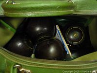 Inside view of green carry bag showing four black vintage lawn bowls with yellow emblem and concentric circle design.