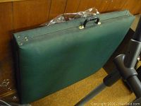 Folding massage table closed, showing green vinyl exterior and black carrying handle.