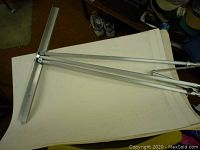 Flip chart easel frame with three aluminum legs folded and the horizontal support bar visible, placed on top of flip chart paper pads.