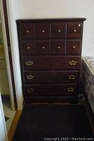 Full front view of the wooden highboy dresser showing the arrangement of drawers and brass knobs and handles.