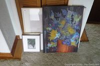Photo showing three pieces of wall decor: an abstract floral oil painting on canvas, a framed bird photo print, and a blank white frame stacked against a wall.