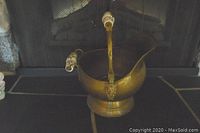 Full view of brass pot showing rounded body, curved spout, and lion head handle with ceramic grips.