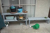 Overall view of three wooden garden benches and various gardening supplies arranged on and around them outside a building.