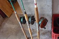 Three fishing rods with Knuckle Buster reels including one Peetz reel, showing wooden handles and full length of rods.