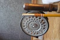 Close-up of the metal fishing reel attached to the vintage rod, showing multiple ventilation holes and wear marks.