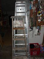 Two stepladders side by side, wooden in front and aluminum behind with visible paint stains and wear on steps and surfaces.