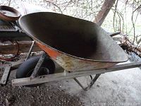 Overall view of metal wheelbarrow with orange paint and wooden handles, showing wear