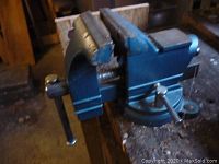 Blue painted metal 3.5 inch bench vise mounted on a wooden workbench showing general wear.