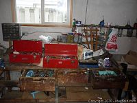 Overall view of workbench with two red metal toolboxes and wooden drawers containing tools and jars of hardware supplies.